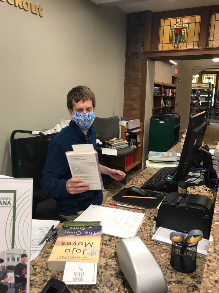 Programming Specialist Zach Heimach scans books while wearing a mask at the main library.