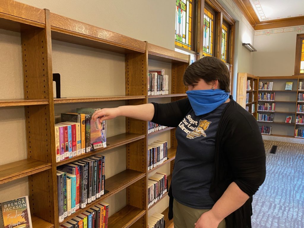 Eckhart Public Library Assistant Director Jenny Kobiela-Mondor picks a book off the shelf at the Main Library. Eckhart Public Library will begin to offer contactless curbside pickup of holds, returns of materials, and document services beginning on Monday, May 11. 